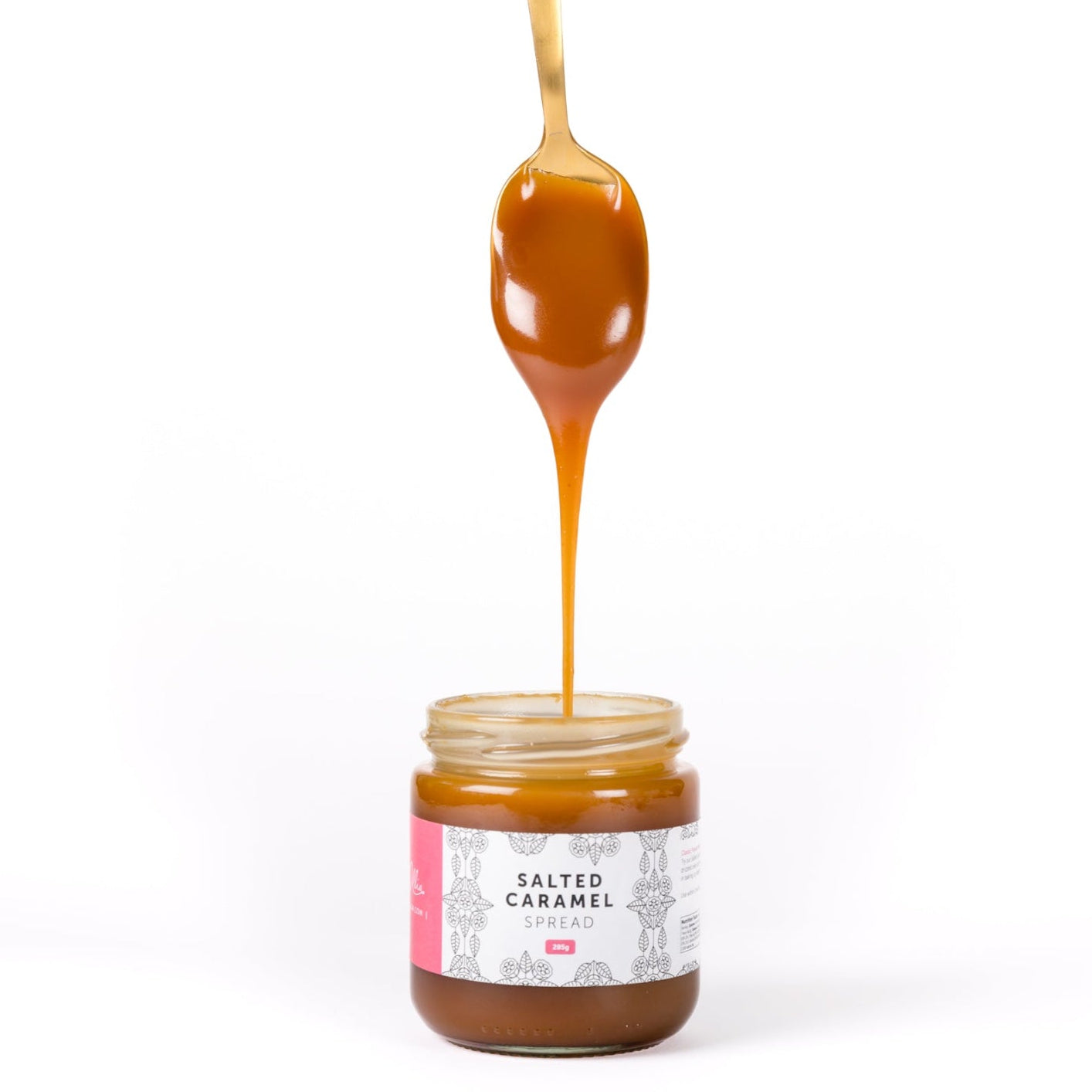Small jar of salted caramel spread with a drizzle of caramel sauce falling from a spoon, on a white background.